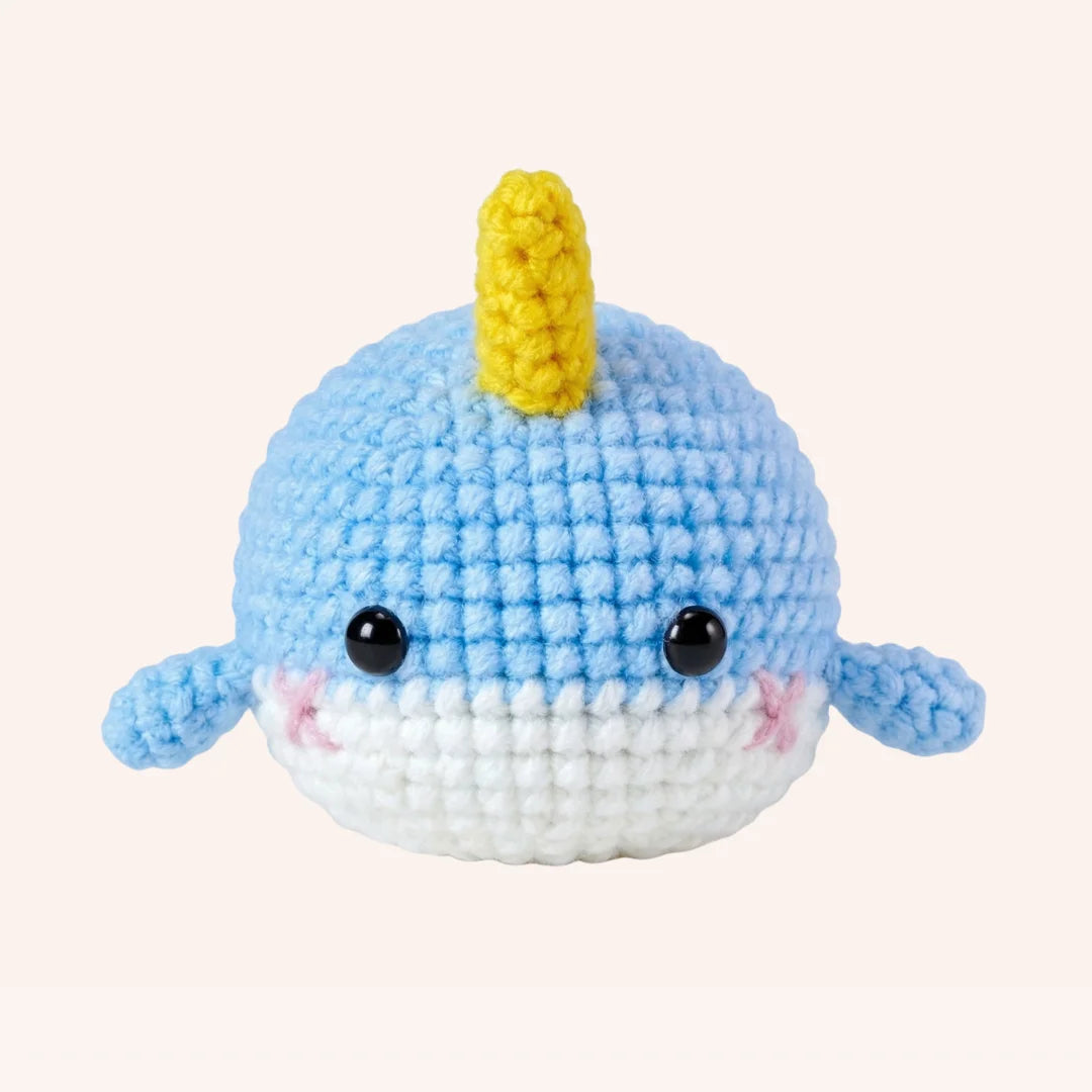 The Little Narwhal crochet amigurumi plush with light blue body, white belly, yellow horn and pink cheeks