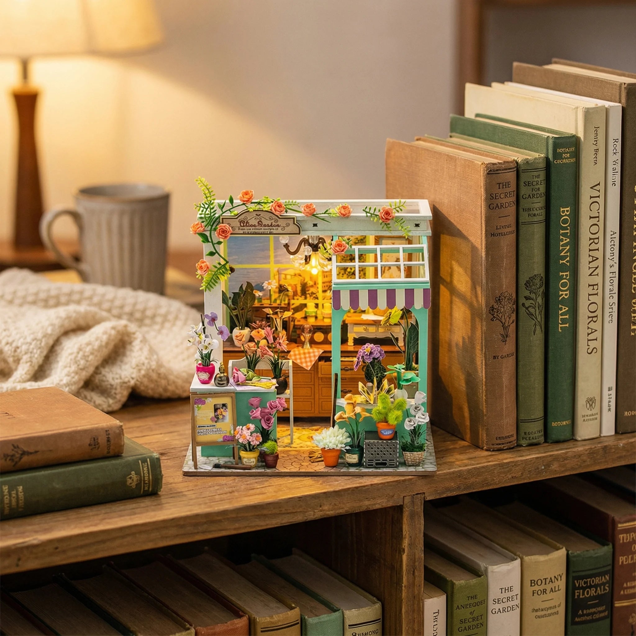 The Blossom Studio miniature flower shop kit displayed on wooden bookshelf surrounded by vintage books and cozy decor
