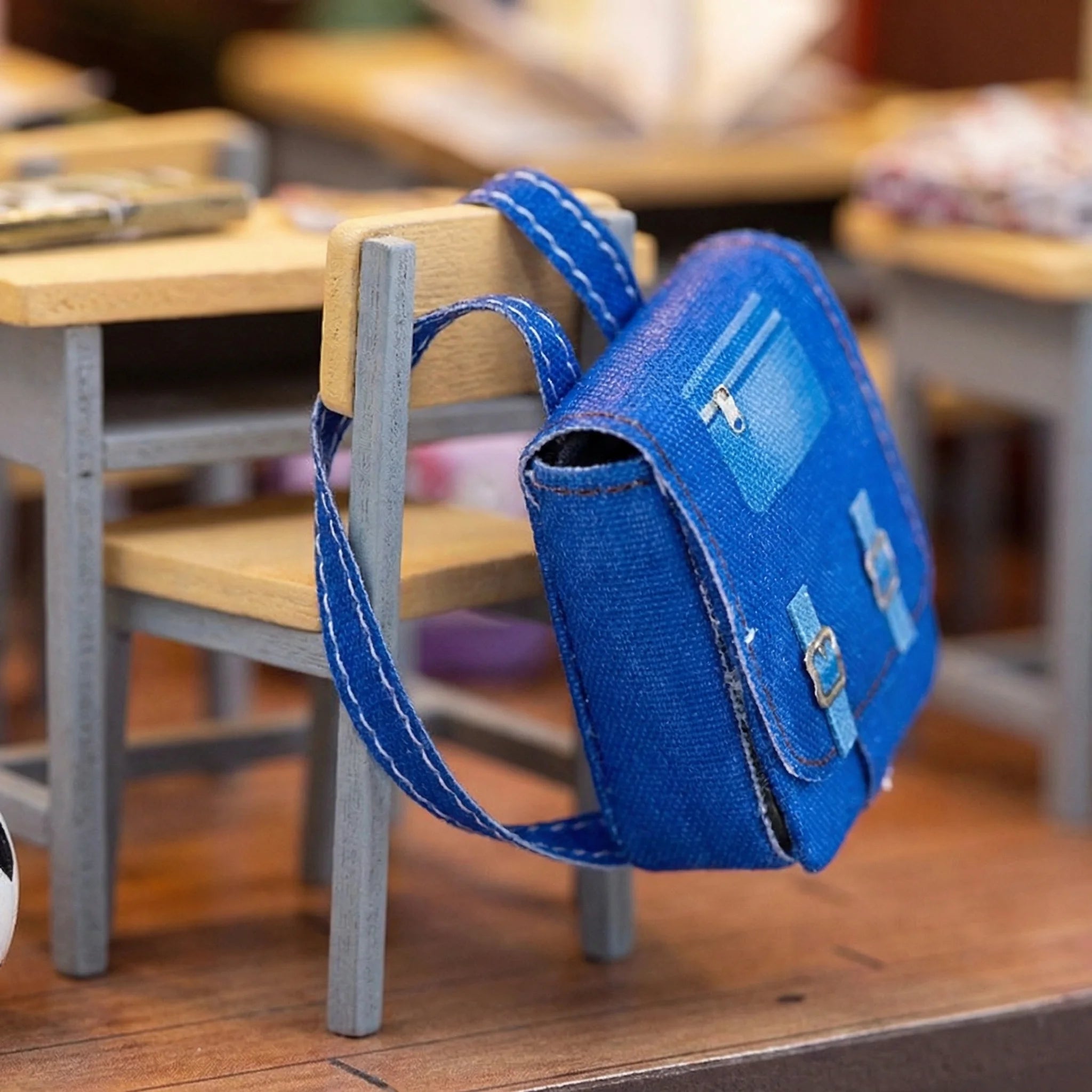 Blue miniature school backpack with white stitching detail hanging on wooden chair from The Homeroom DIY crochet kit