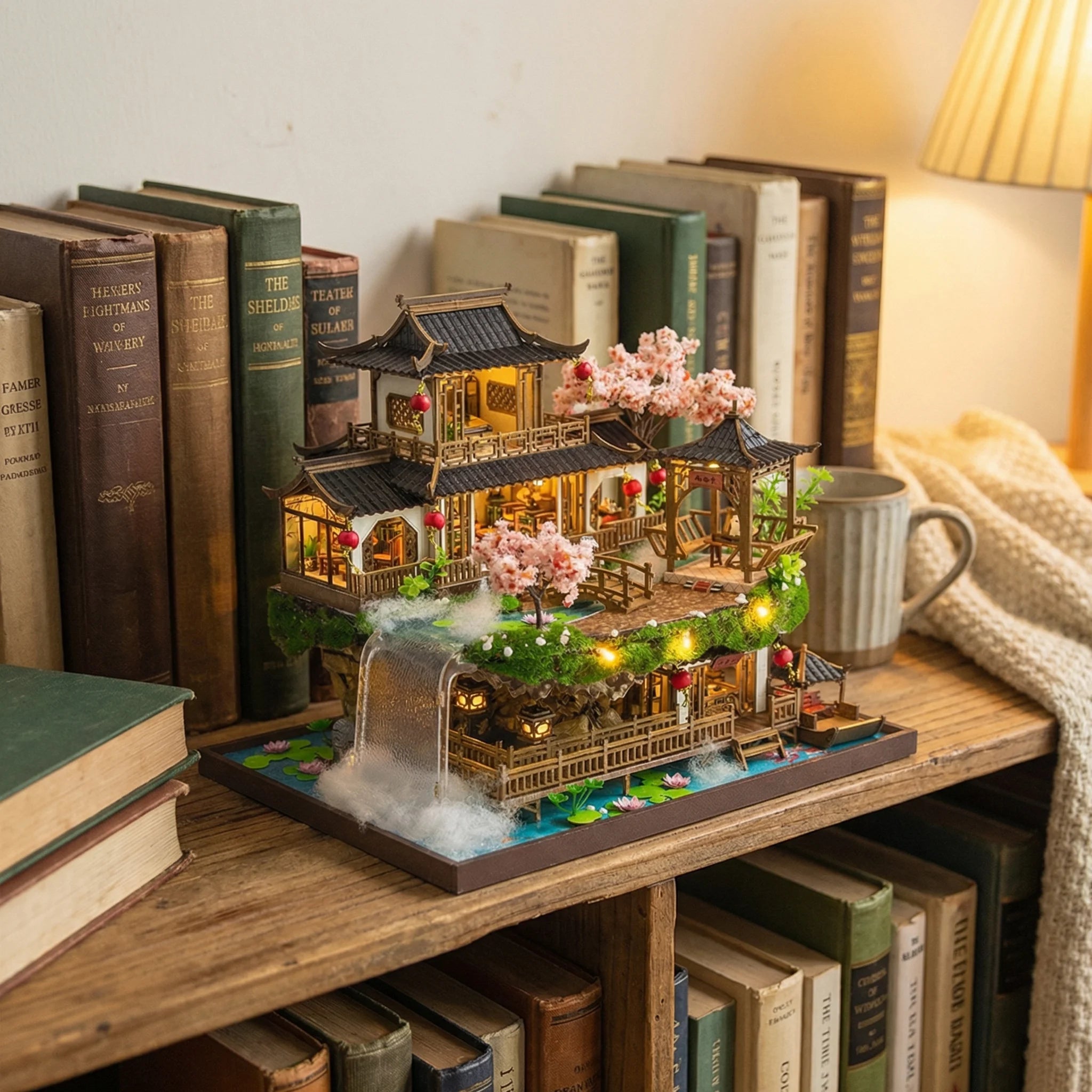 The Lotus Pavilion miniature house kit displayed on bookshelf with lit lanterns and cherry blossoms DIY model