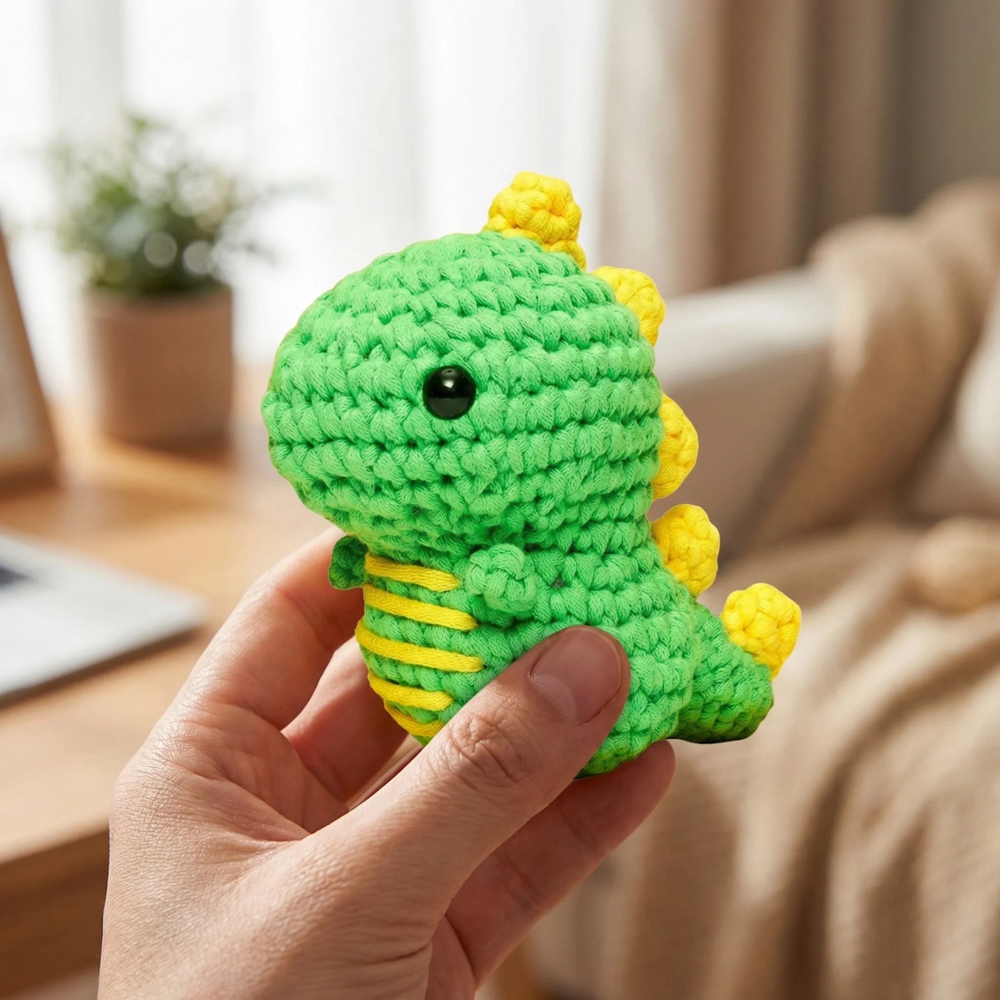 Hand holding The Little Dragon green and yellow mini crochet amigurumi plush toy in cozy home setting