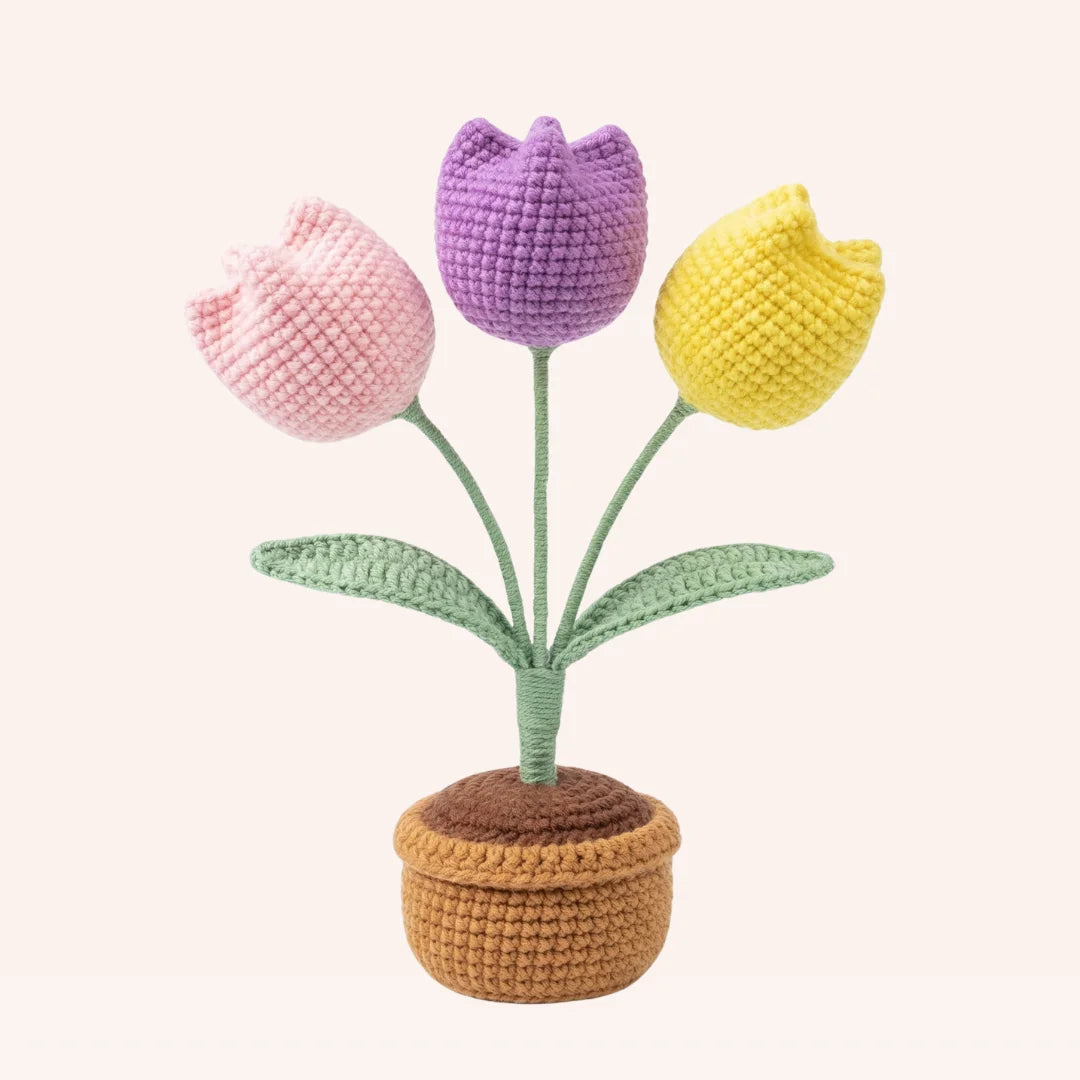 The Tulip Garden crochet amigurumi kit featuring three pastel tulips in pink, purple, and yellow with green leaves in a ta...