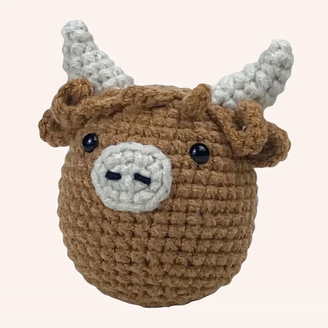 The Highland Cuddle DIY crochet kit featuring a miniature brown highland cow amigurumi with gray horns and black bead eyes