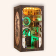 The Clockwork Apothecary DIY book nook kit on a cream background, brass gears and emerald glowing potion shelves
