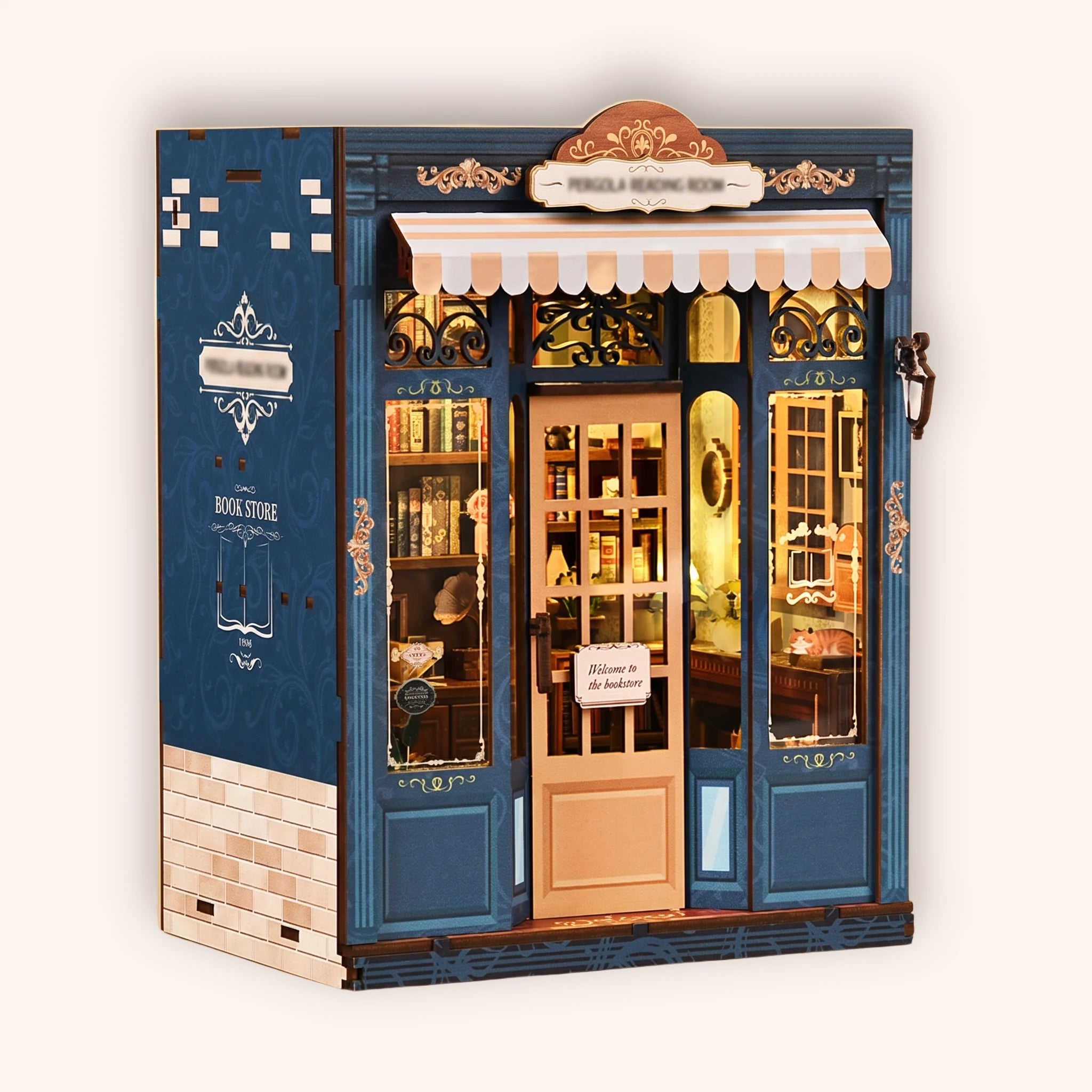 The Corner Bookshop DIY book nook kit, navy storefront with a striped awning and glowing display window, on a soft cream background