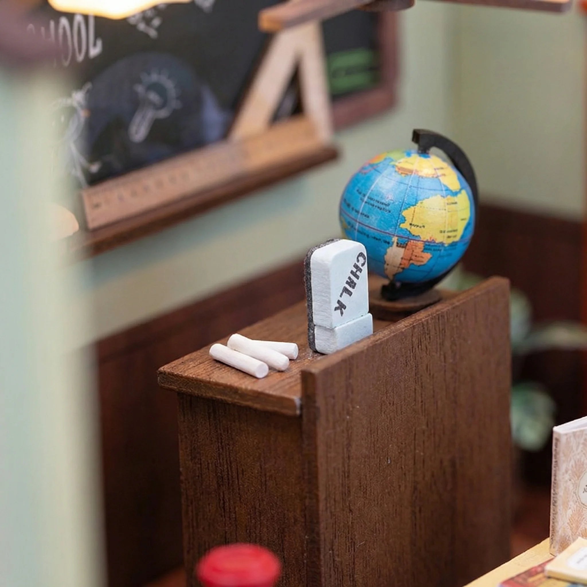 The Homeroom miniature classroom scene showing wooden desk with tiny globe, chalk, and chalkboard from DIY crochet kit