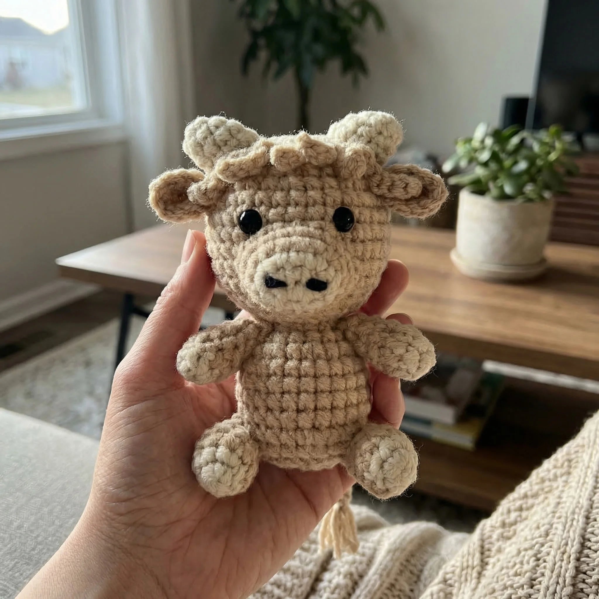 Buttercup the Cow mini crochet amigurumi held in hand showing palm-sized scale in cozy living room setting
