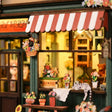 Close-up of the striped awning and storefront with hanging flower basket and window boxes of The Aura Verde Flower Room