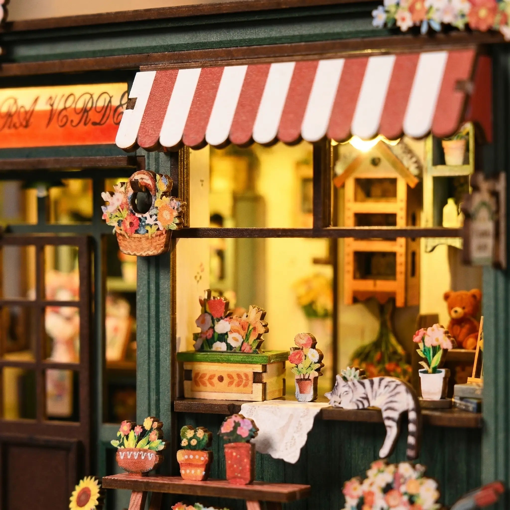 Close-up of the striped awning and storefront with hanging flower basket and window boxes of The Aura Verde Flower Room