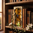 The Fairy Glen treehouse book nook slotted on a bookshelf between books at dusk, interior glowing warm amber