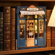 The Corner Bookshop book nook slotted on a shelf between books, glowing warm at dusk