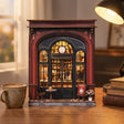 The Coffee Corner miniature on a warm wood desk with a coffee mug and books