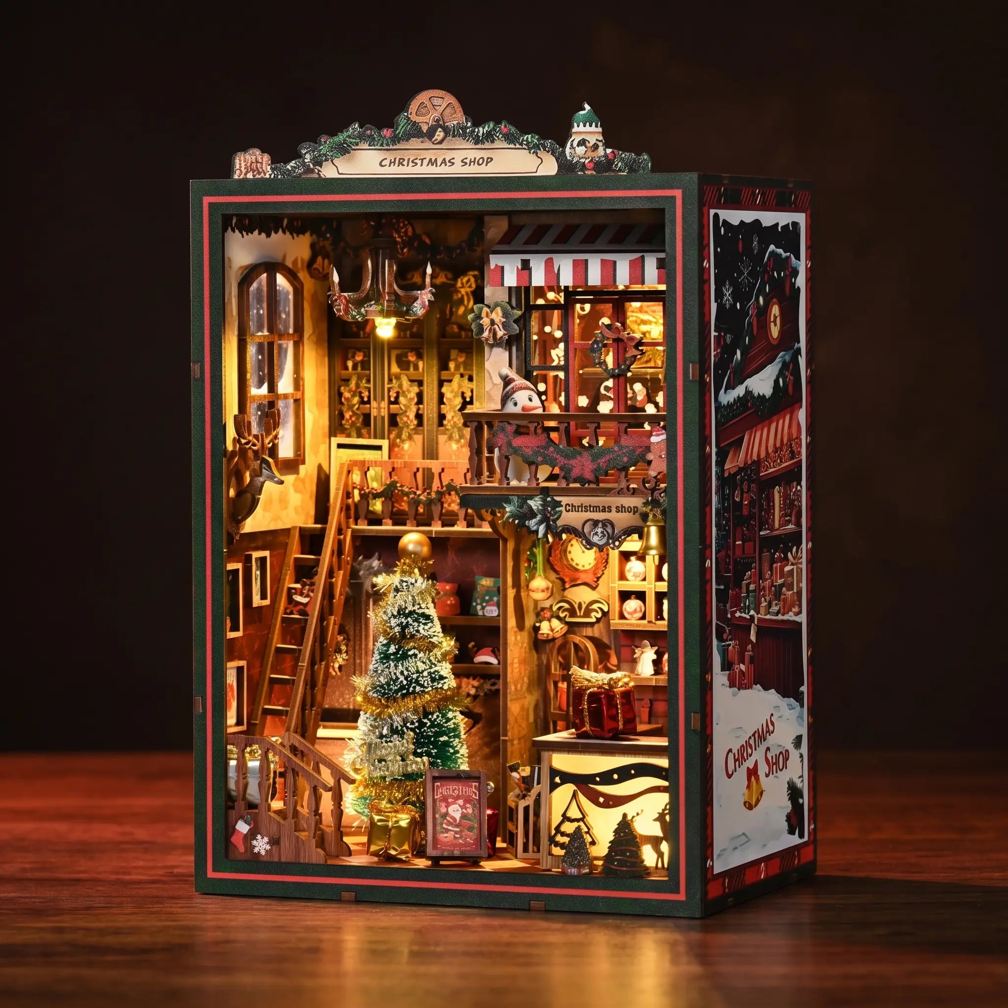 The Christmas Shop DIY book nook kit, lit festive shop interior on a dark walnut surface