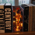 The Lantern Alley book nook slotted on a shelf between books, glowing at dusk