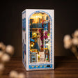The Aegean Alley miniature Greek book nook, front three-quarter view on a dark backdrop with warm LED lighting