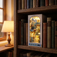 The Aegean Alley miniature book nook slotted on a shelf between books with warm LED lighting