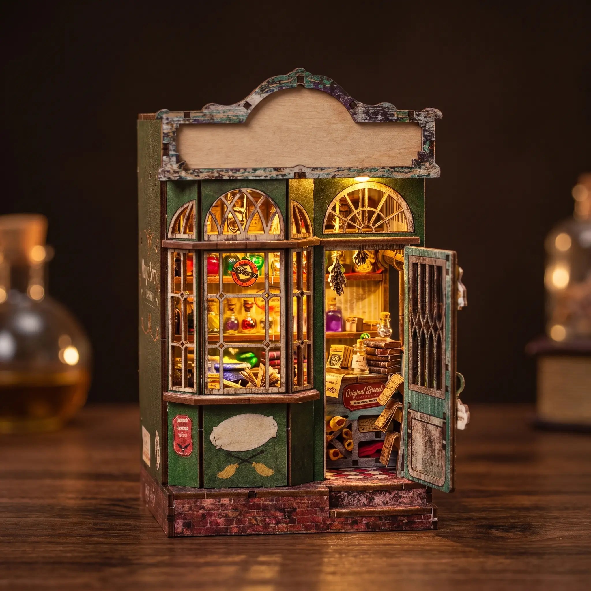 The Enchantment Shop DIY book nook kit, lit green wizard's magic shopfront on a dark backdrop