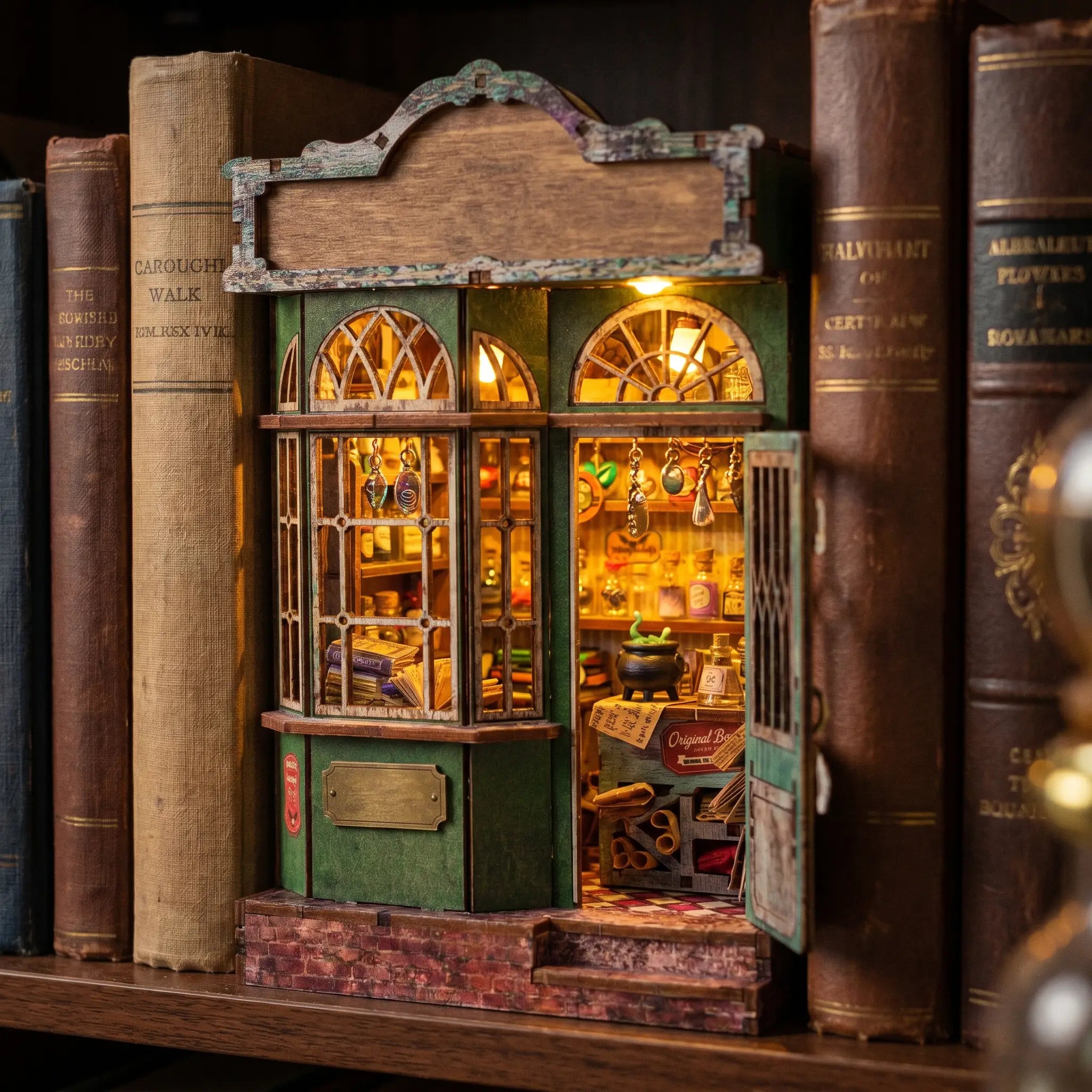 The Enchantment Shop book nook glowing on a bookshelf between books at dusk