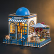 The Santorini Café miniature Greek coffee shop with its blue domed roof, front three-quarter view on a dark backdrop with warm LED lighting