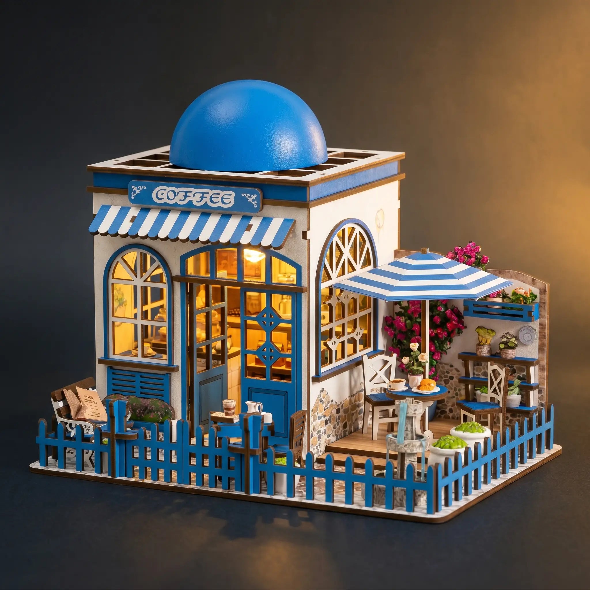 The Santorini Café miniature Greek coffee shop with its blue domed roof, front three-quarter view on a dark backdrop with warm LED lighting