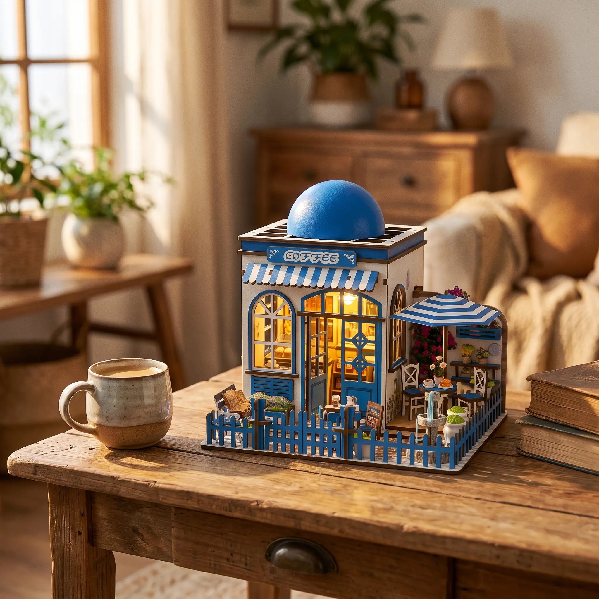 The Santorini Café miniature with blue domed roof on a warm wood desk beside a coffee mug and books
