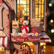 Snowman in a top hat among gift boxes on The Candy Cane Cottage ledge