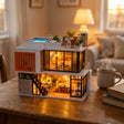 The Glass Villa miniature kit lit up on a wooden desk beside a mug of tea