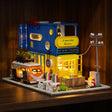 The Roadside Bistro miniature kit glowing on a dark walnut shelf at night