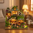 The Mossgrove Cottage lit up on a wooden desk at dusk beside tea and books