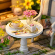 Detail of the tea table: gold-rimmed teacup, cake stand and pink flowers