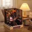 The Seer's Parlor roombox on a wooden desk at dusk beside a mug of tea