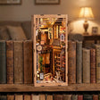 The Cat's Alley book nook glowing on a bookshelf between books
