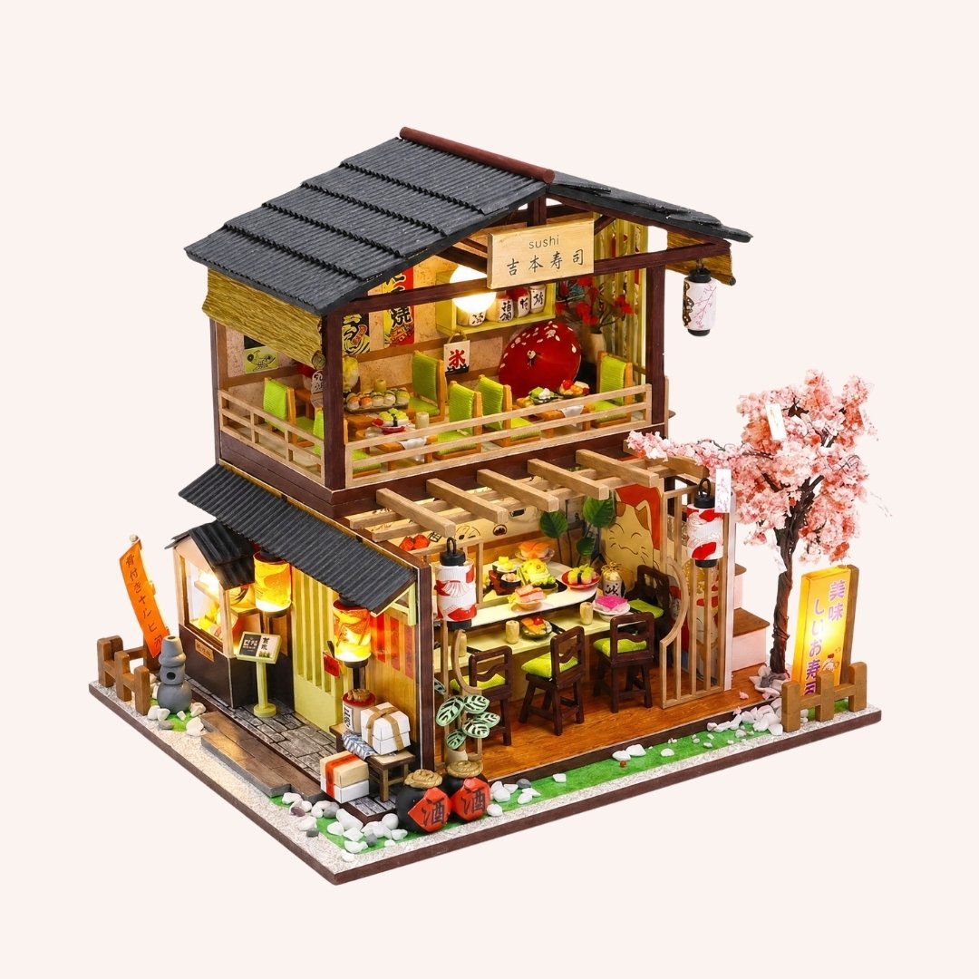 Hands assembling The Sakura Sushi Bar kit, fitting the sushi counter, lanterns, tile roof and cherry blossom tree, ending with the LED lanterns switching on