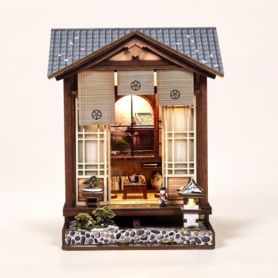 Hands assembling The Lantern House miniature kit, ending with the LED lights switching on