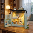 Hands assembling The Mint Gables miniature kit, ending with the lights switching on
