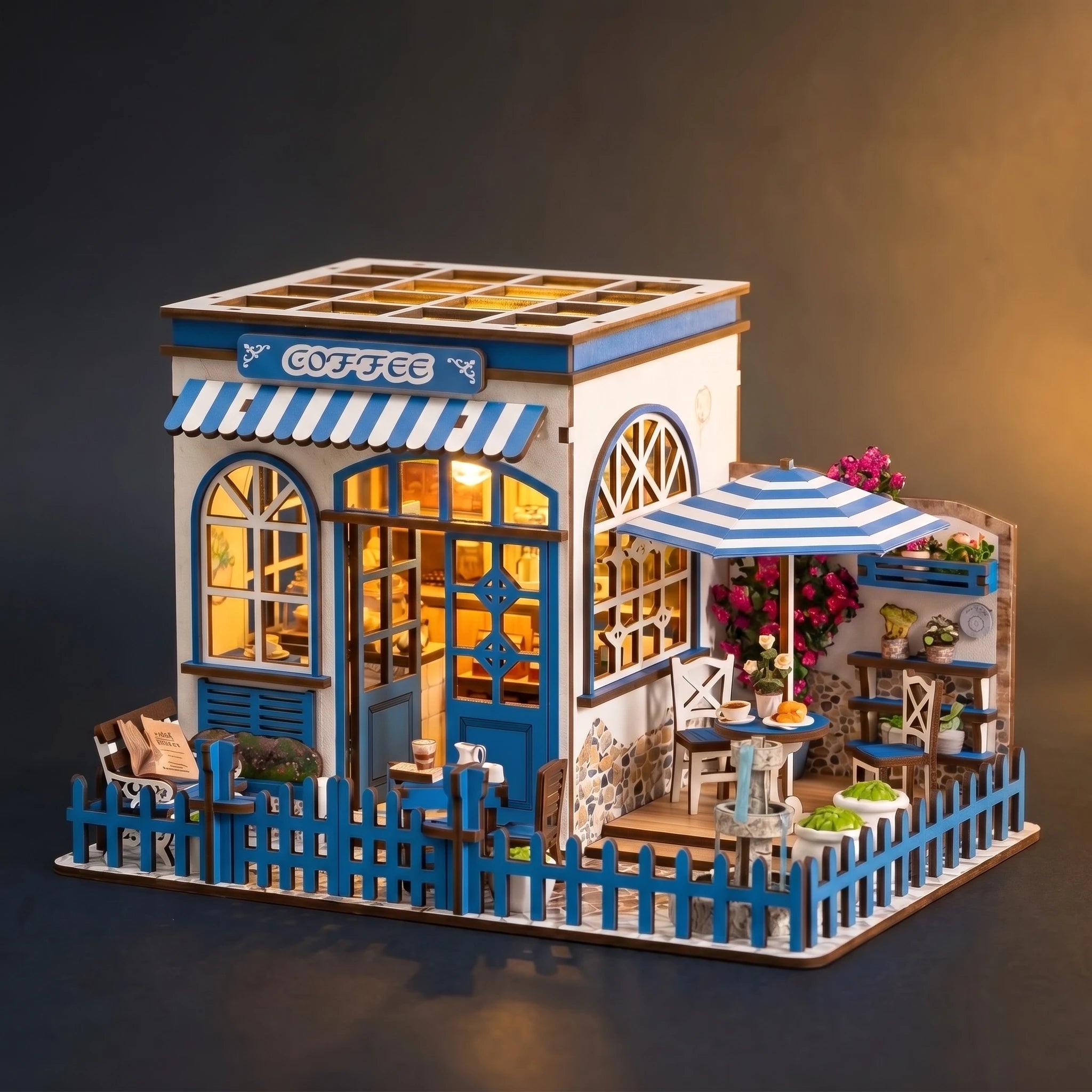 The Santorini Café miniature Greek coffee shop, front three-quarter view on a dark backdrop with warm LED lighting