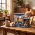 The Santorini Café miniature on a warm wood desk beside a coffee mug and books