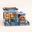 The Santorini Café miniature blue-and-white Greek coffee shop roombox on a soft cream background with warm LED lighting