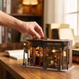 A hand placing a piece on The Alchemist's Cafe, shown in real-world scale