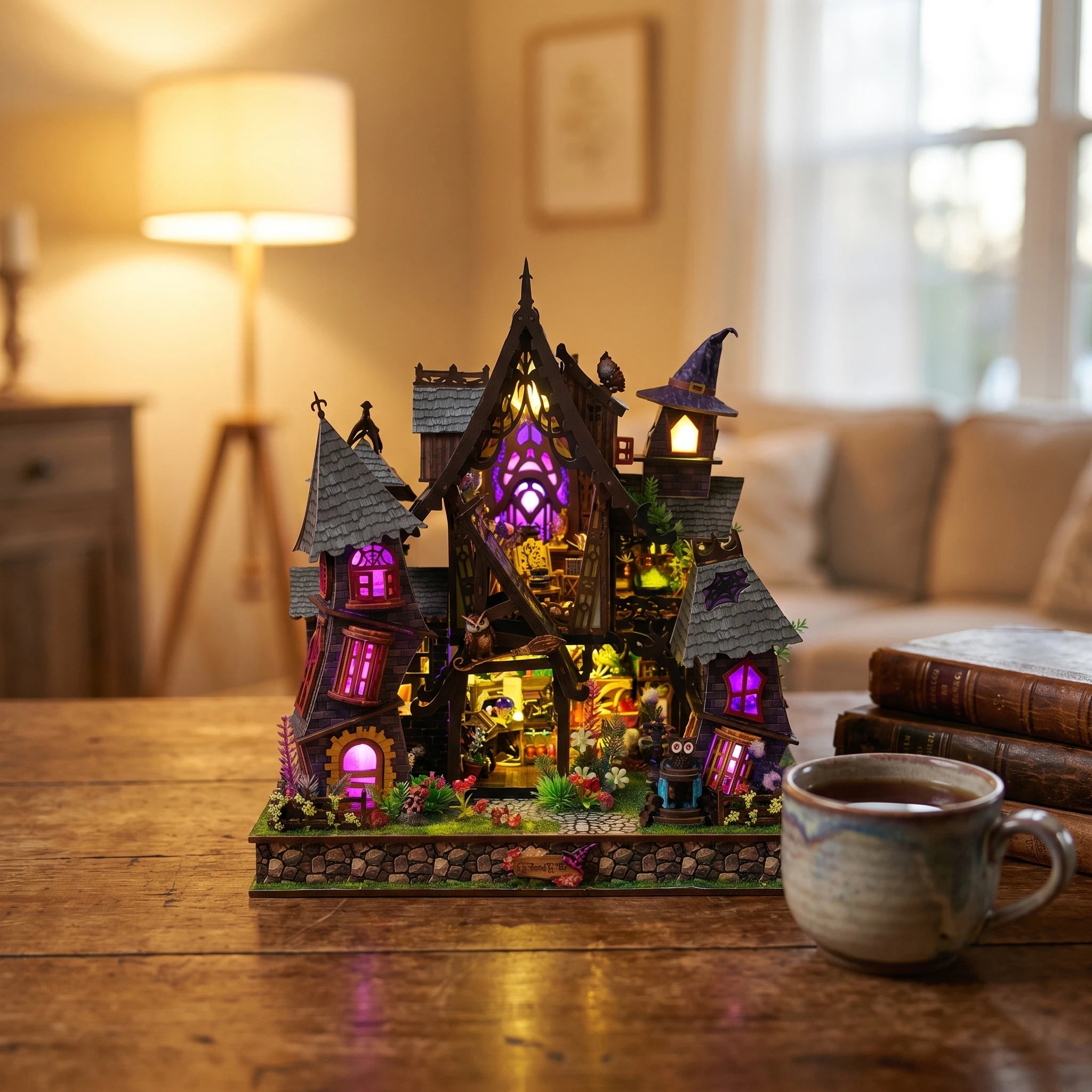 The Crooked Cauldron lit on a desk at dusk beside tea and books