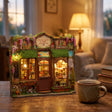 The Dollhouse Shop lit up on a desk at dusk beside a mug of tea