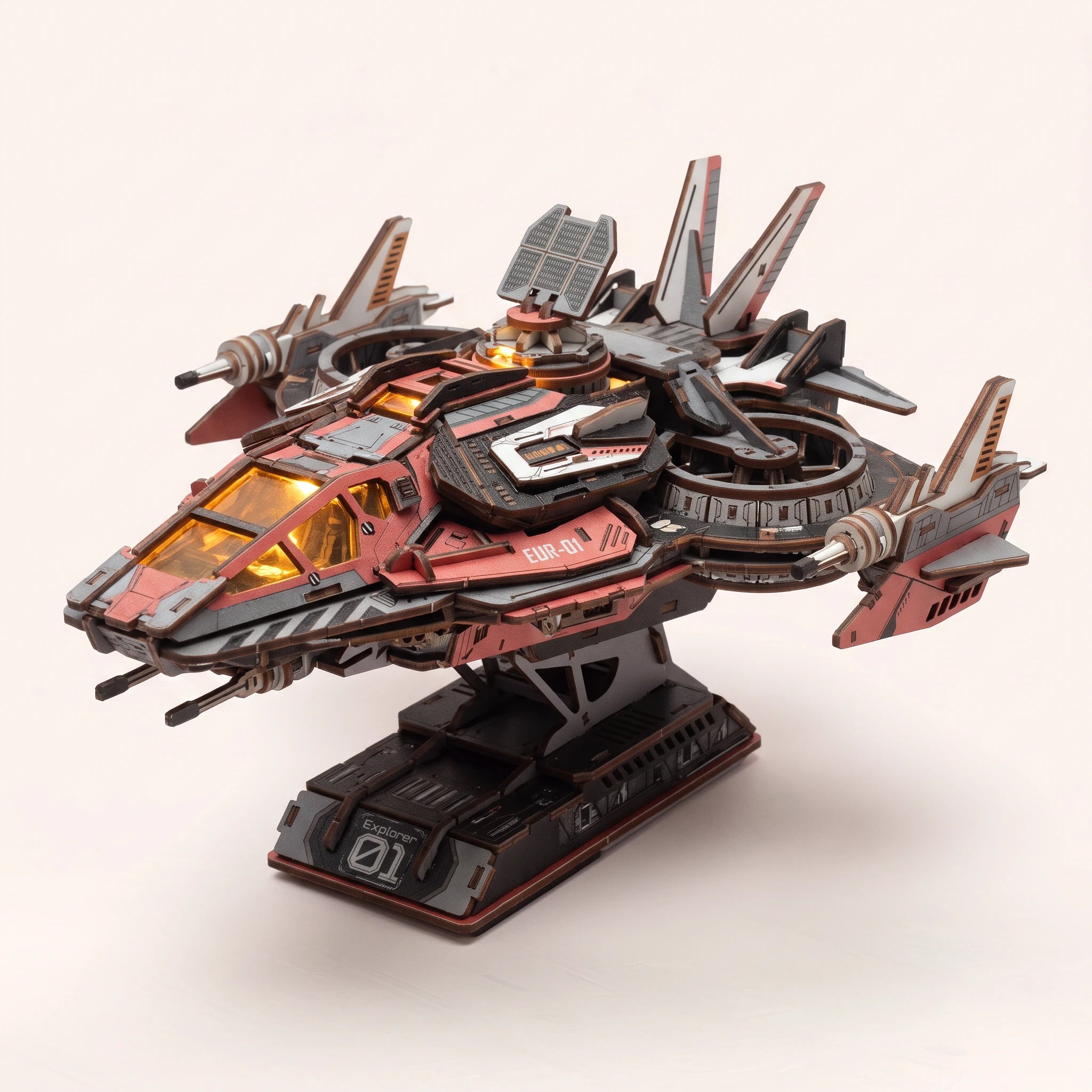 The Explorer One wooden starship kit on its stand, cockpit lit, on a pale blush background