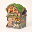 The Mossy Hollow DIY book nook kit with LED lights glowing on a pale blush studio background