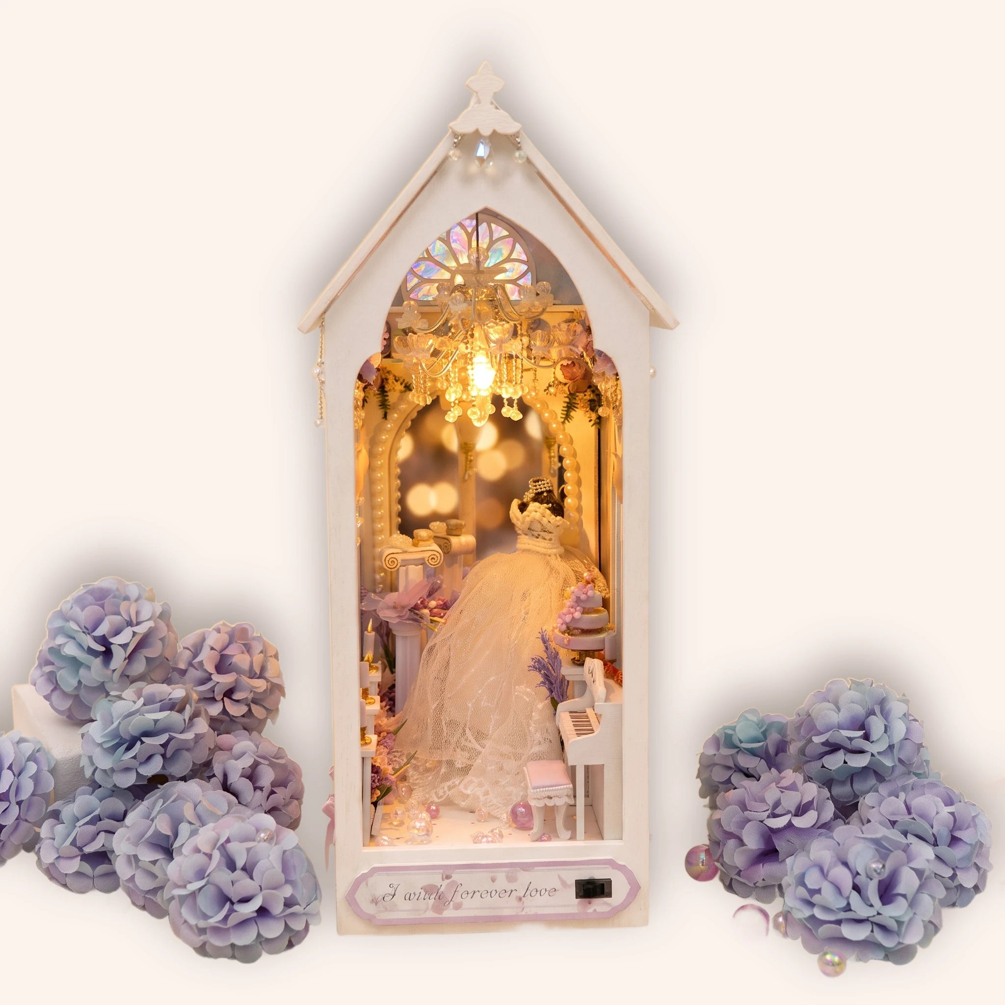 The Wedding Chapel DIY book nook kit, a white gothic wedding chapel with a stained-glass rose window and crystal chandelier glowing warm